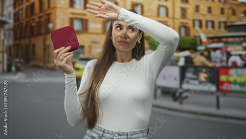 Photography Woman holding a small red wallet and raising her hand to block the camera on a busy city street in casual jeans; annoyance privacy