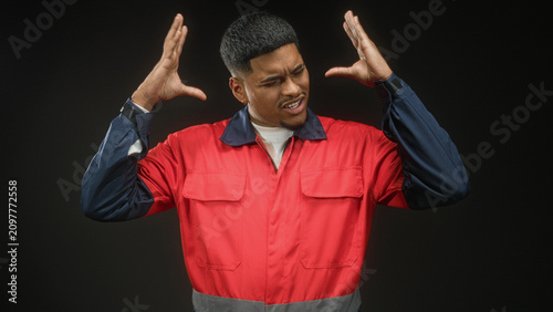 Foto Man in red uniform grips his head with both hands, grimacing in studio; frustration strain fatigue work