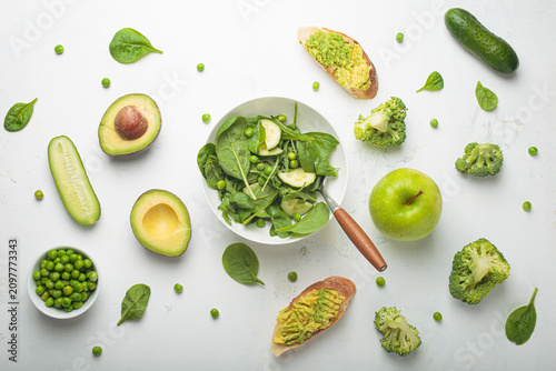 Fresh salad bowl, avocado toasts, raw green vegetables fruit white background top view, diet