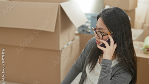 Bild auf Leinwand Woman holding smartphone to ear and hand near face among stacked cardboard moving boxes in building; concern