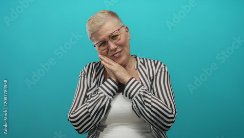 фотографія Woman with hands clasped in prayer wearing glasses and striped shirt in studio against turquoise backdrop; hopeful reflection