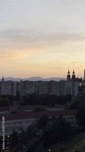 The sun sets behind buildings and mountains, creating a colorful sky with orange and purple hues
