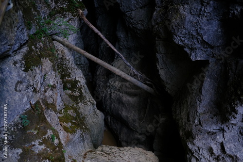 Dark cave opening with wooden log and mossy rocks in mountain gorge