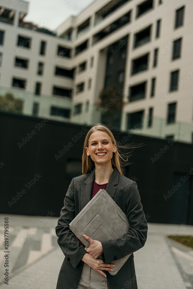 Fototapeta premium Businesswoman standing outdoors smiling with laptop sleeve