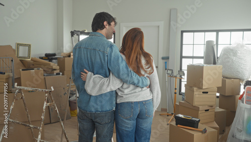 Canvas Print Man embraces woman with arm around waist among stacked moving boxes in a building; hopeful new start