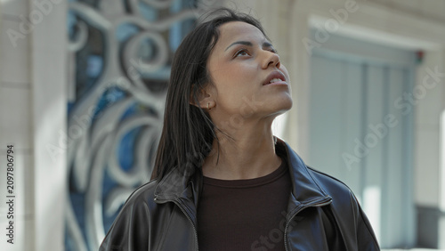 Foto Woman young looking up with exposed neck and leather jacket before ornate metal facade of a city building; quiet wonder
