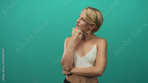 Obraz na płótnie Blond woman with hand on chin and crossed arm in studio wearing white camisole showing midriff, looking sideways; contemplative reflection