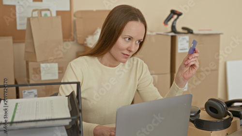 Konstfotografi Woman holding creditcard near laptop at desk with stacked packages and shipping label in building; entrepreneurial focus