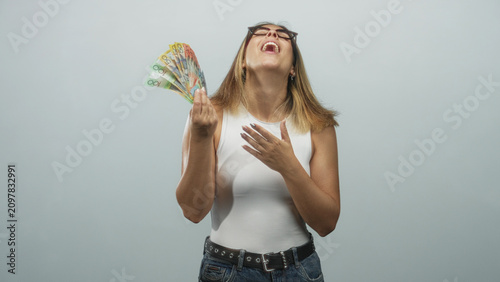Fotografía Woman kissing and fanning australian dollars with hand on chest in a studio setting, wearing glasses and white sleeveless top; joy celebration