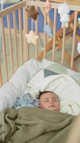 Fotografía Boy sleeping in wooden crib with face relaxed, wrapped in green blanket and plush toy in nursery building; peaceful rest