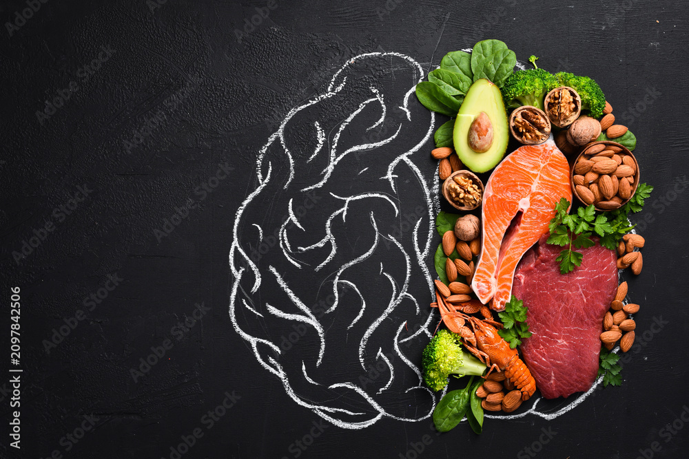 Fototapeta premium Concept of healthy food for the brain: fish, meat, nuts, vegetables and greens. Brain drawing with chalk on a blackboard. Top view. On a black background.