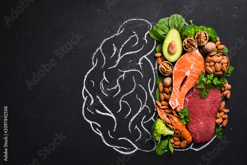 Concept of healthy food for the brain: fish, meat, nuts, vegetables and greens. Brain drawing with chalk on a blackboard. Top view. On a black background.