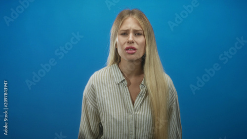 Foto Woman with long blonde hair in striped shirt grimacing with puckered lips against blue studio backdrop; disgust discomfort