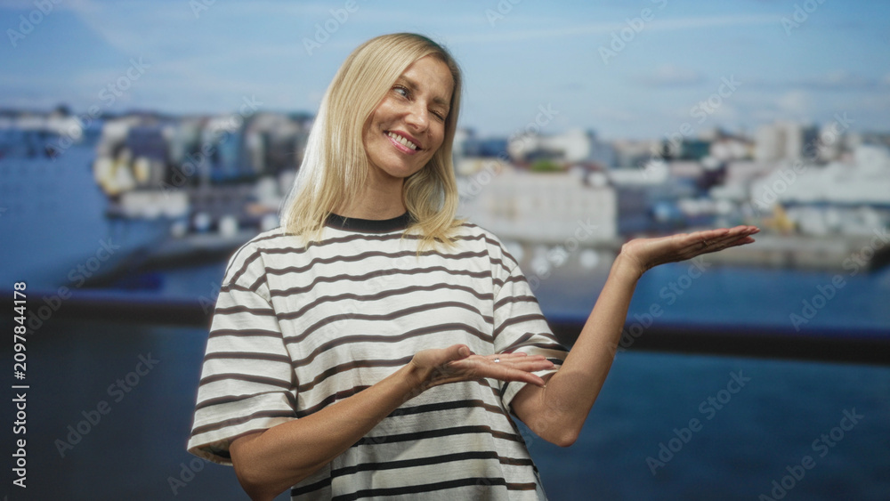 Fototapeta premium Woman smiling with eyes closed, hands presenting a gentle gesture in studio with blurred harbor backdrop; serenity.