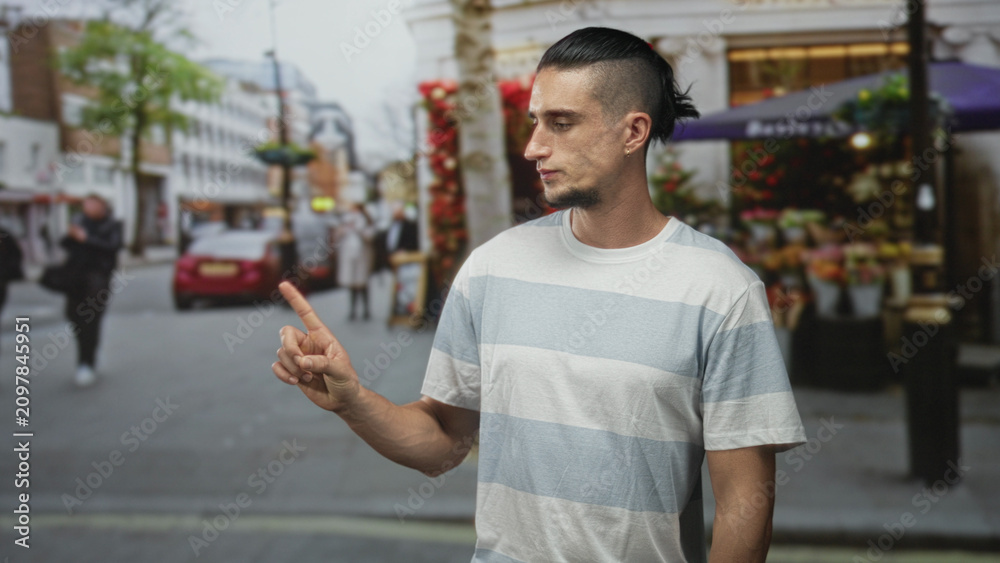 Obraz premium Man gazes sideways at flower stall, striped t shirt and bare forearm visible, standing on a busy street; quiet contemplation.