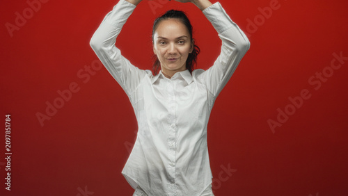 Принти на полотні Young woman forming heart with hands over head in studio against red backdrop, smiling and turning subtly; love joy
