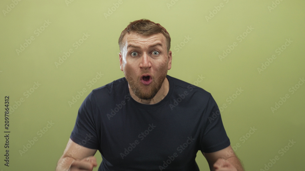Fototapeta premium Young caucasian overweight man with raised fists, tongue out and bearded face cheering in studio with olive green background; excitement celebration win.
