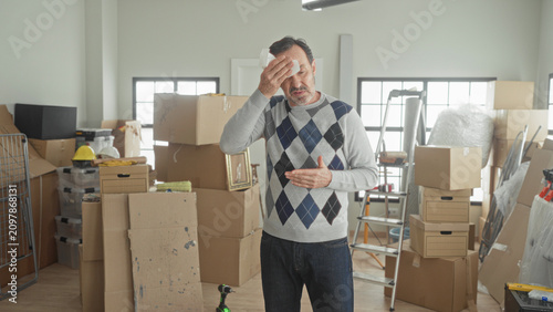 Bild auf Leinwand Man middle aged wiping face with tissue and hand on chest beside stacked cardboard boxes in a building during unpacking in new home; fatigue