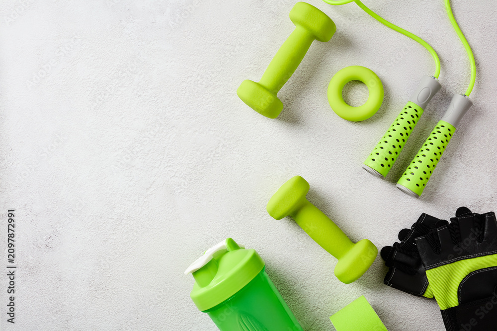 Naklejka premium Assorted green sport equipment and workout accessories on the right side of a textured gray background with copy space. Flat lay.