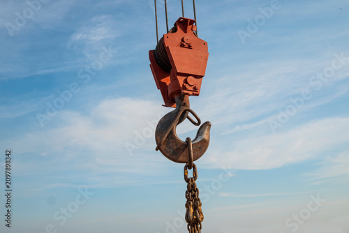 Canvas Print Close-up of a construction crane hook hanging from steel cables against a blue sky with soft clouds