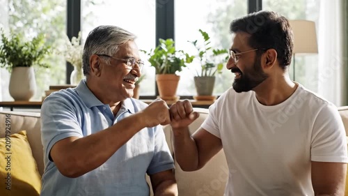 Happy father and adult son greeting each other with fist bump while spending quality family time at home