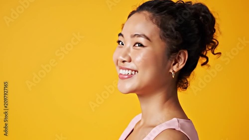 Happy Young Asian Woman Smiling in Side Profile Portrait Against Bright Yellow Studio Background