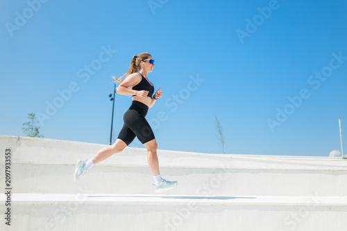Bild auf Leinwand Energetic woman running swiftly under a bright blue sky during a sunny afternoon