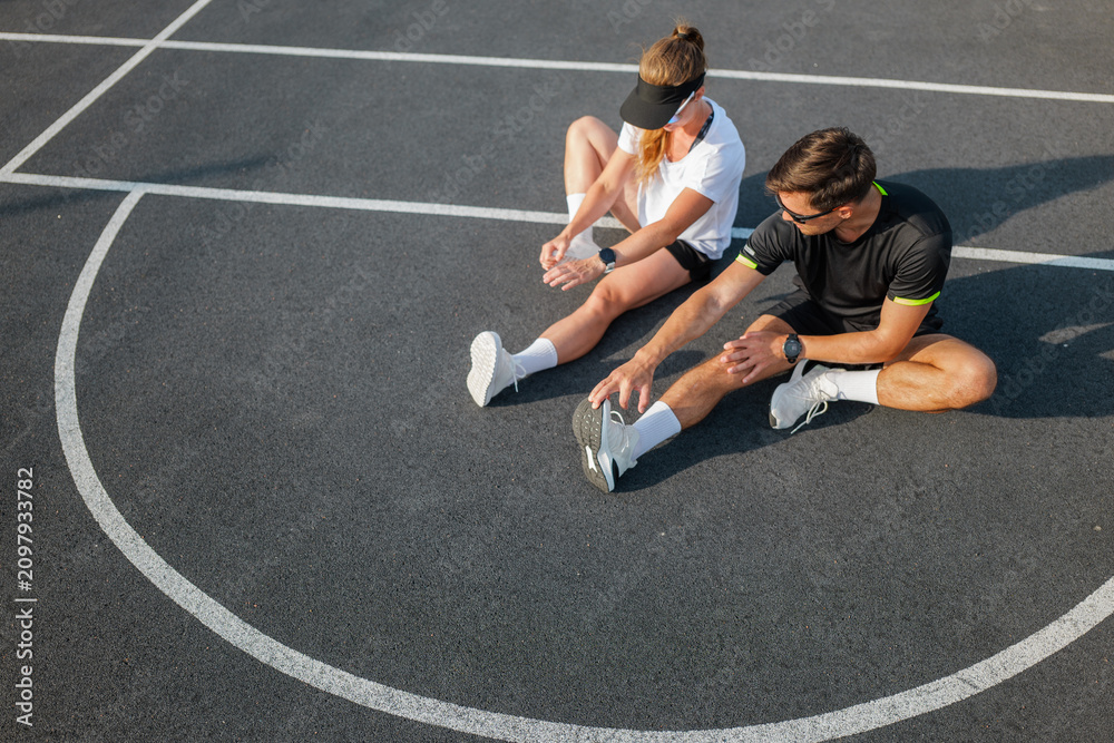 Obraz premium Couple stretches together on a sunny day at the basketball court, preparing for an afternoon of fitness and fun