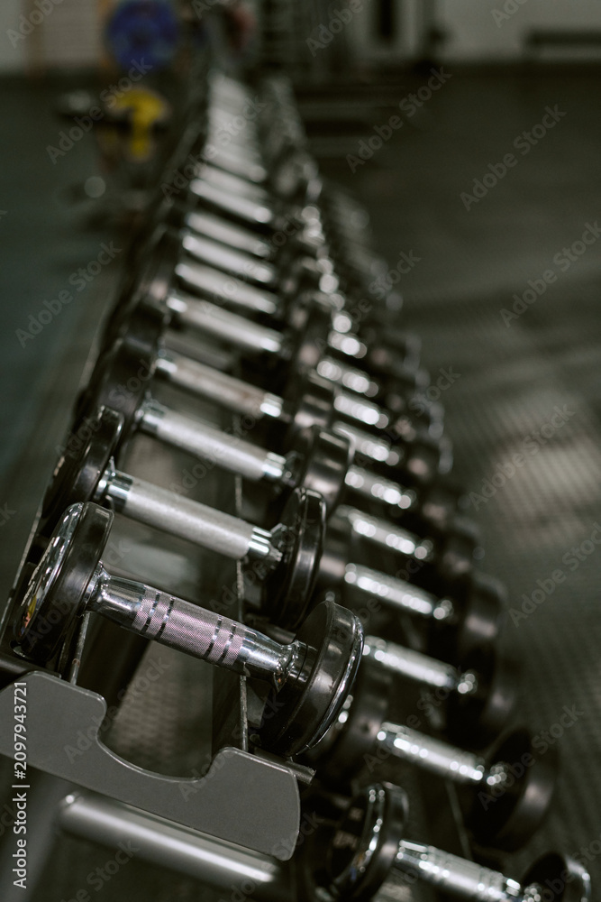 Fototapeta premium Vertical shot of dumbbells lining gym rack, supporting strength training, fitness routine, muscle building concept. Ideal for workout promotion, wellness branding, sports ads