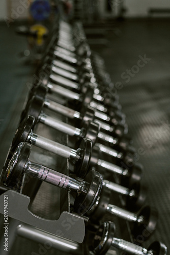 Vertical shot of dumbbells lining gym rack, supporting strength training, fitness routine, muscle building concept. Ideal for workout promotion, wellness branding, sports ads