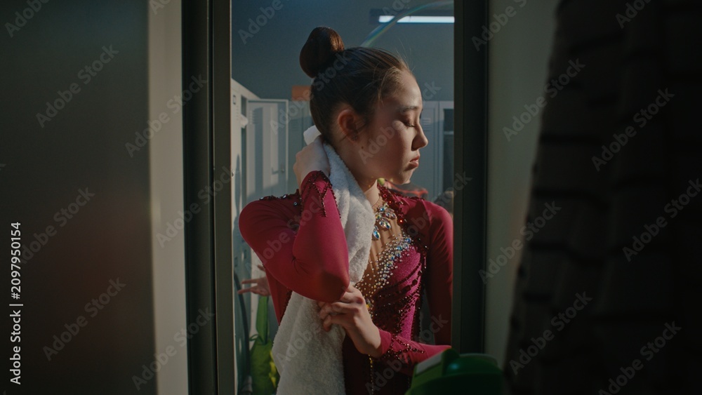 Obraz premium Tired Young Gymnast in Burgundy Crystal Embroidered Costume Opens Locker After Performance, Drinks Water, and Gently Wipes Sweat From Neck and Forehead With Towel. Reality of Competitive Gymnastics.
