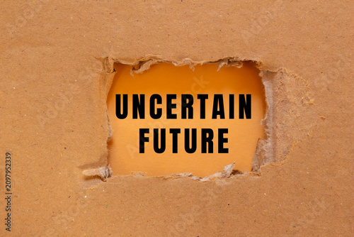 Konstfotografi Cardboard paper torn into a hole, revealing the bold text uncertain future on an