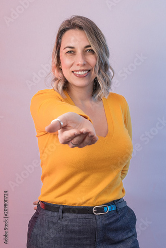 Smiling woman extending an open hand toward the camera, representing invitation, offering, help, support, welcome, trust and human connection.