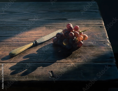 Rustic Dark Wood Table with a Single Cluster of Deep Purple Wine Grapes and a Vintage Brass Corkscrew Representing Autumn Wine Harvest, Moody Still Life, and Classic Winemaking Concept