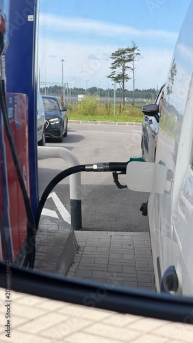 Foto A fuel nozzle is inserted into the gas tank filler of a white commercial van at a gas station, with the fuel pump visible