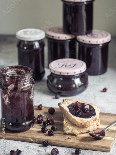 Homemade blackberry jam jars with toast and fresh blackberries on rustic wooden board