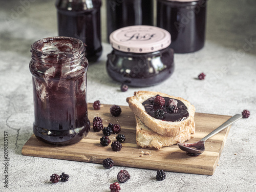 Homemade blackberry jam jars with toast and fresh blackberries on rustic wooden board