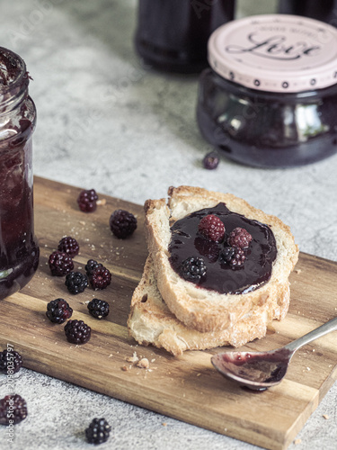 Homemade blackberry jam jars with toast and fresh blackberries on rustic wooden board