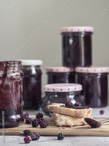 Homemade blackberry jam jars with toast and fresh blackberries on rustic wooden board
