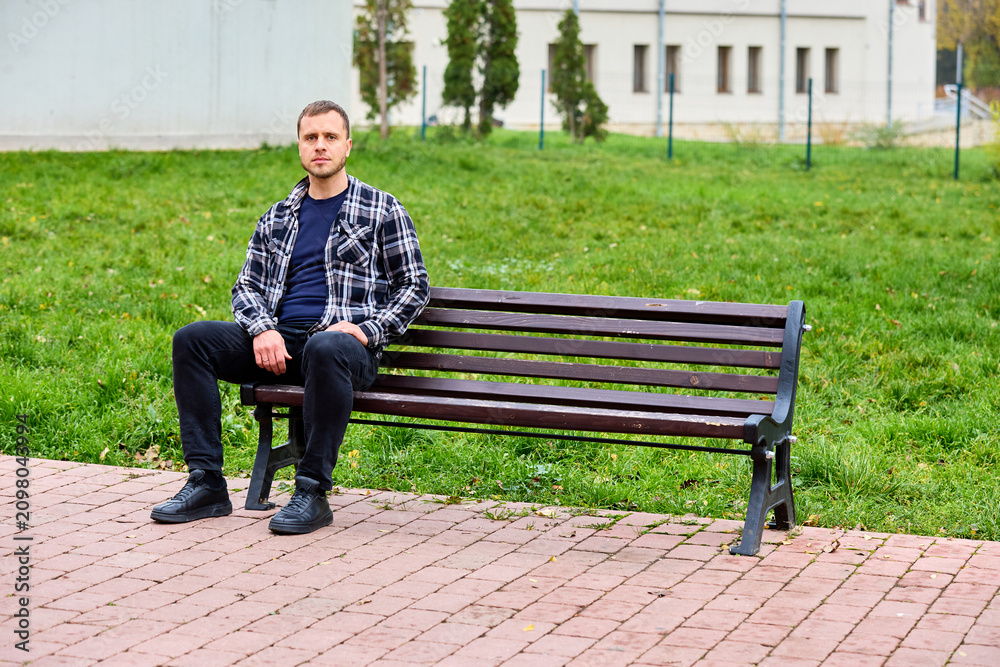 Obraz premium Young man sits calmly on park bench