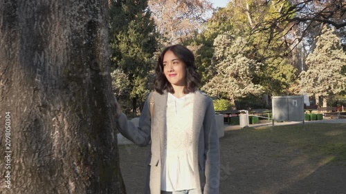 Beautiful Latina woman looking straight ahead next to a tree in a park.
