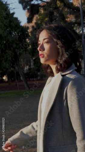 Young businesswoman walking alone in the park at sunset and searching people. Vertical video