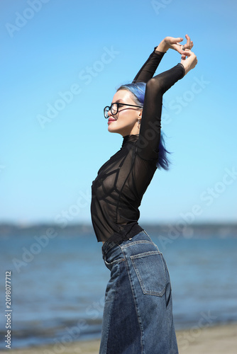 Stylish young woman with blue hair posing on sunny beach