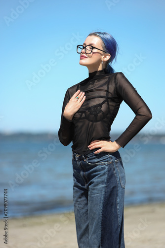 Stylish young woman with blue hair posing on sunny beach