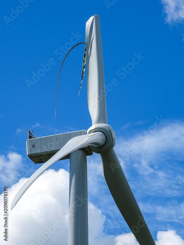 Close Up of Damaged Wind Turbine with Broken Blade Against Blue Sky and White Clouds in Daylight View