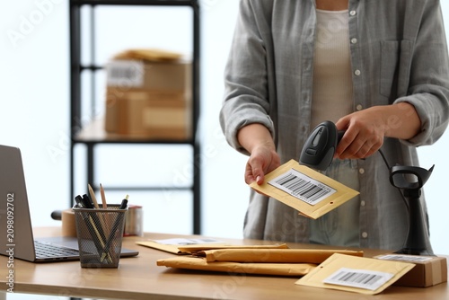 Bild auf Leinwand Post office worker with scanner reading barcode on envelope at wooden desk indoors, closeup