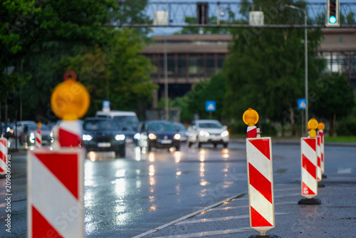 Temporary traffic delineator with amber warning beacon marking a lane closure during urban road reconstruction on a wet roadway, highlighting traffic engineering safety