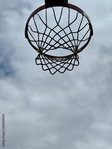 Direct low angle view of a basketball hoop and net isolated against a cloudy sky background. Concept of targeting goals, aspiration, motivation, and outdoor street basketball.