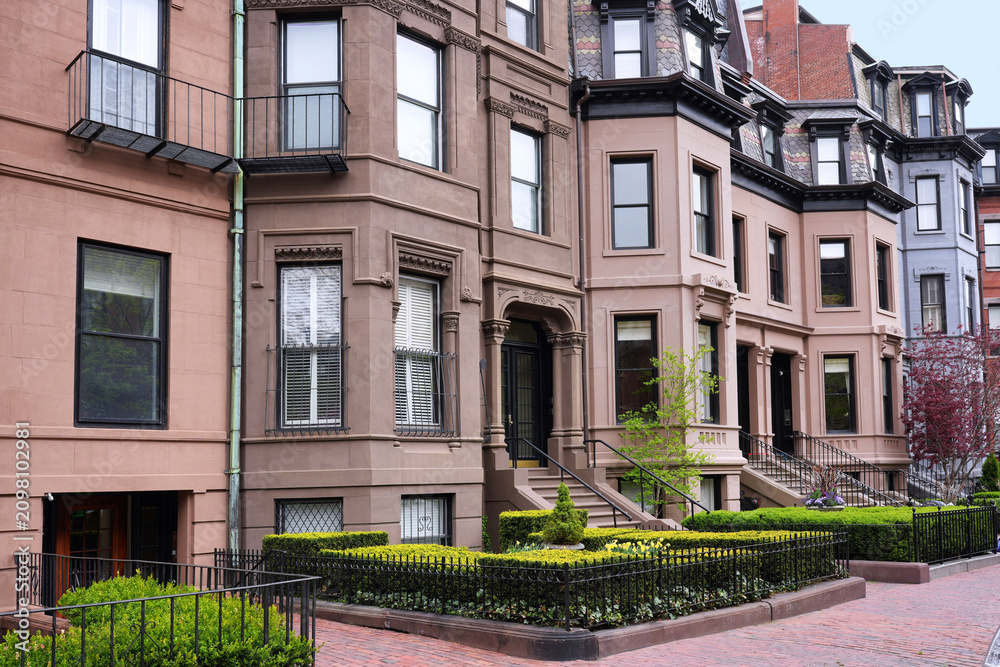 Naklejka premium Row of old brownstone townhouses with bay windows and small front gardens