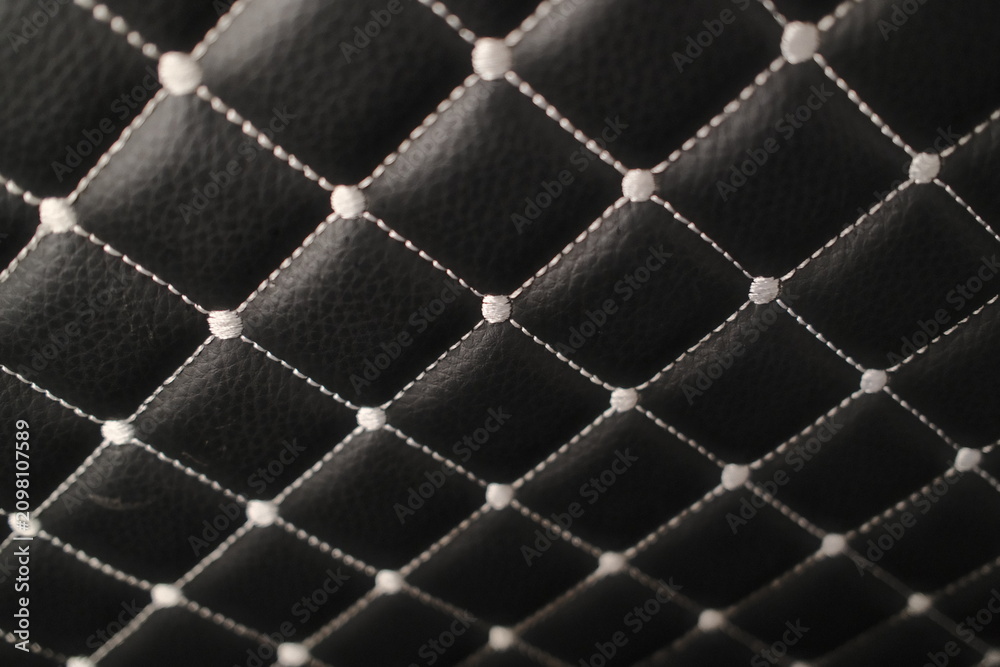 Obraz premium Close-up of black textured leather featuring a decorative diamond pattern formed by white contrast stitching. Each intersection has a raised point.